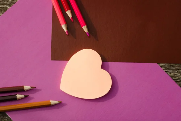 Colored pencils and stickers with pink hearts on a brown and lilac background. School stationery flat lay