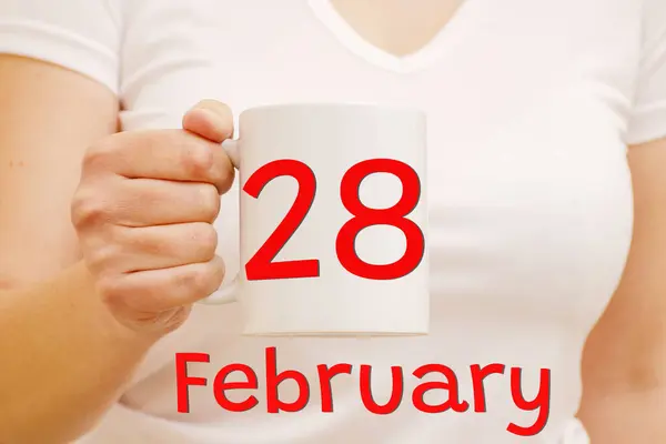 Celebración y concepto de negocio. Taza blanca con inscripción roja 28 de febrero en una mano femenina. —  Fotos de Stock