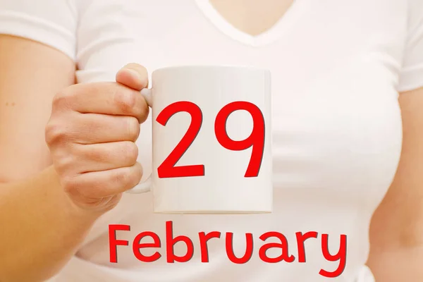Celebración y concepto de negocio. Taza blanca con inscripción roja 29 de febrero en una mano femenina. —  Fotos de Stock