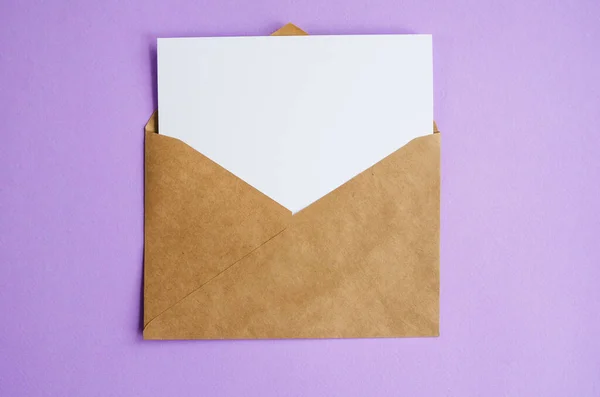 Kraftpapier envelop met een wit vel papier op een lila ondergrond. De flat lag met kopieerruimte. Valentijnsdag concept — Stockfoto