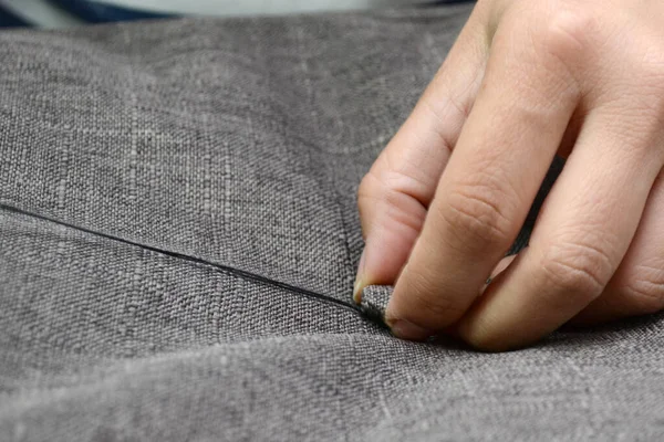 A seamstress with black thread sews on a gray fabric button, horizontal photo. Small business concept.