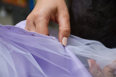 Kadın stüdyoda çalışıyor, küçük işletme konsepti. Terzi leylak kumaştan dikiş dikiyor. Yatay fotoğraf.