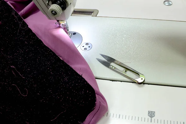 Work tools seamstress. Pink and black fabric on a sewing machine. Tailor\'s workplace, cloth and tongs. Small business concept.