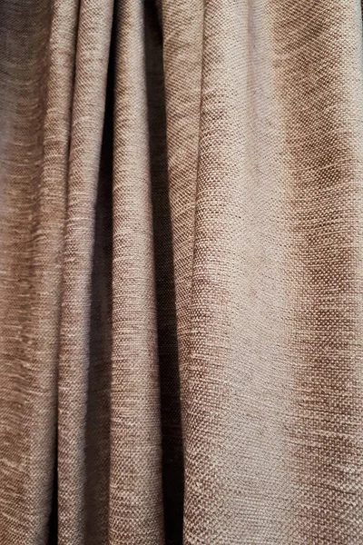 Material och tyger. Närbild av en ljusbrun gardin i tunna och tjocka vertikala veck tillverkade av tät tyg. Texturerade abstrakta bakgrunder och tapeter. — Stockfoto