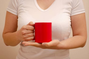 Beyaz tişörtlü bir kadın elinde kırmızı bardakla fotokopi çekiyor. Ev konforu ve reklamın yatay fotoğrafı
