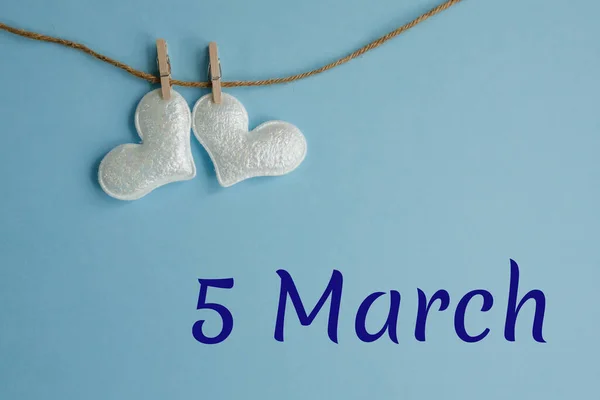 5 Mart 'ın anısına mavi arka planda çamaşır mandallı beyaz kalpler, düz yatış. Tatil takvimi kavramı