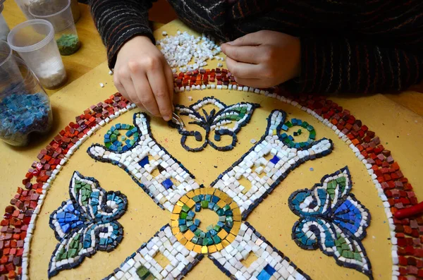 Cımbızlı kadın eller mozaik atölyesine küçük bir resim yaydılar. Küçükten kaynaklı yetenekler. İçinde bir desen olan kırmızı bir daire çiziyorum. Seçici odak.