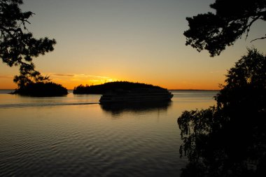 Gölün üzerinde gün batımı, adaların üzerinde güneş batışı, geminin siyah silueti. Doğanın güzel fotoğrafı.