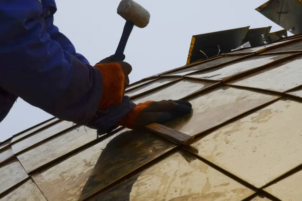 The assembly of the gilded dome of the Orthodox church. The master in working gloves, collects parts of the dome. With a rubber mallet and a wooden board.