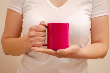 Beyaz tişörtlü bir kadın elinde pembe bir kupa tutuyor. Ev konforu ve reklamın yatay fotoğrafı