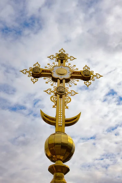 Cross on a background of the sky with gray clouds. Golden orthodox cross close-up. Religion concept, vertical photo.