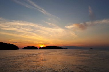 Adaların arkasındaki gölün üzerinde gün batımı, açık bir gökyüzünün açıklarında. Gemi ufuktan çok uzakta. Seyahat ve tatil kavramı.