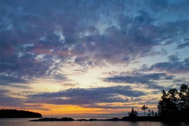 Ladoga Gölü üzerinde, Karelia 'da gün batımı. Bulutlu mavi bir gökyüzünün yatay fotoğrafı. Güneş ufukta batıyor.