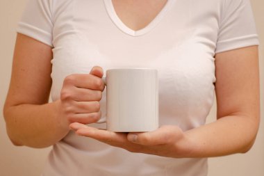 Beyaz tişörtlü bir kadın elinde beyaz bir kupa tutuyor. Ev konforu ve reklamın yatay fotoğrafı