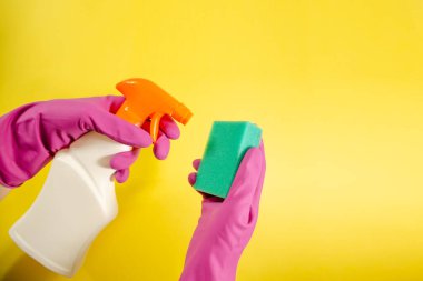 Pembe eldivenli kadın eller sarı arka planda beyaz sprey ve sünger tutuyor. Kopya alanı ile temizlik kavramı