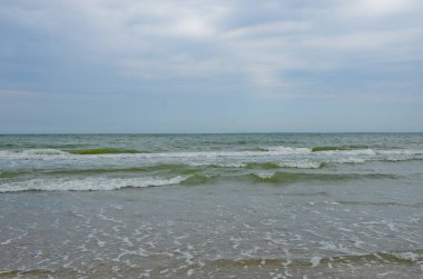 Yaz bulutlu bir günde deniz manzarası. Küçük dalgalar kumsalda yuvarlanıyor.