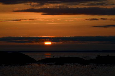 Sakin bir gölün üzerinde güzel bir gün batımı. Bulutlar arasındaki güneş ufkun ötesine geçer. Seyahat kavramı