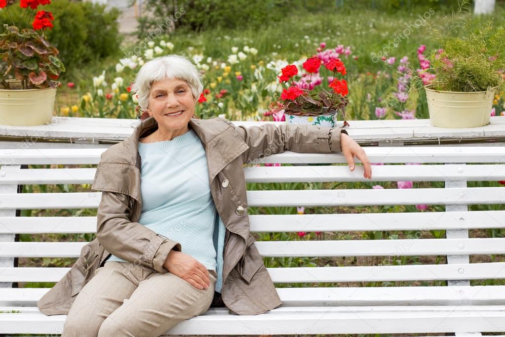 beautiful cute elderly woman sitting on a park bench with flower
