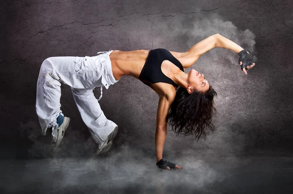 Young beautiful athletic woman dancing modern dance hip-hop on wall background with smoke smoke