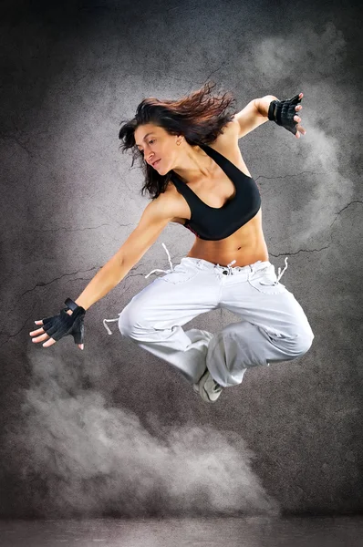 Young beautiful athletic woman dancing modern dance hip-hop on wall background with smoke smoke