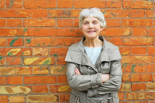 Elderly woman senior standing near a brick wall on the backgroun — Stok fotoğraf