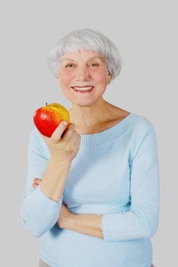 elderly woman with red apple in hands on a light background in the studio, mother, grandmother