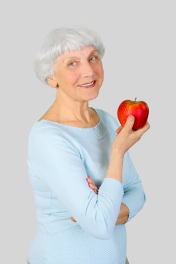 elderly woman with red apple in hands on a light background in the studio, mother, grandmother