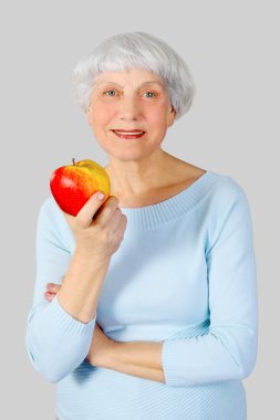 elderly woman with red apple in hands on a light background in the studio, mother, grandmother