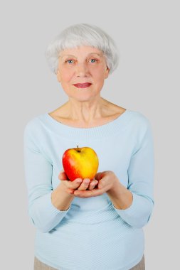 elderly woman with red apple in hands on a light background in the studio, mother, grandmother