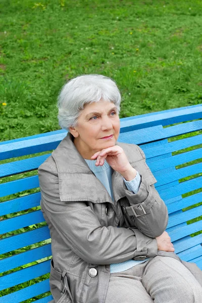 Smuk sød ældre kvinde sidder på en park bænk blå - Stock-foto