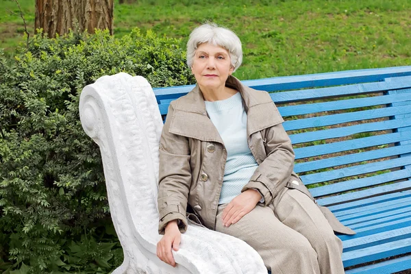 beautiful cute elderly woman sitting on a park bench blue