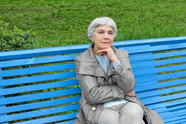 Beautiful cute elderly woman sitting on a park bench blue — Stok fotoğraf