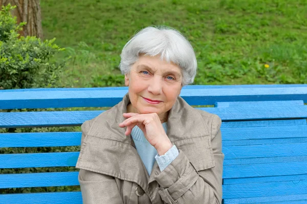 beautiful cute elderly woman sitting on a park bench blue