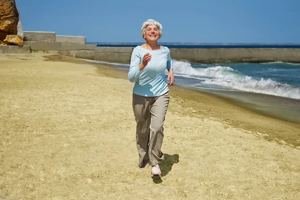 elderly happy woman running on the beach along the coast near the sea