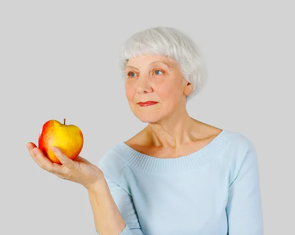 Elderly woman with red apple in hands on a light background in the studio, mother, grandmother — Stok fotoğraf