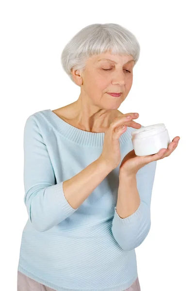 Очаровательная пожилая женщина наносит косметический крем на лицо для ухода за кожей лица на белом фоне — стоковое фото