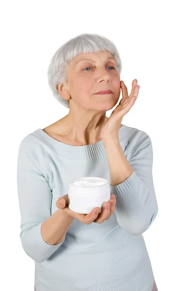 Γοητευτικό ηλικιωμένη γυναίκα που την καλλυντική κρέμα στο πρόσωπό της, για την περιποίηση του δέρματος του προσώπου σε λευκό φόντο — Φωτογραφία Αρχείου