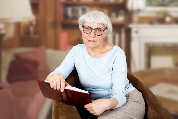 Mutlu güzel yaşlı kadın ile kitap ve gözlük bir sandalyede oturuyor. Anne. Büyükanne
