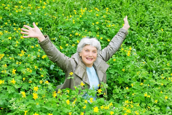 Glædelig smuk ældre kvinde sidder arme udstrakt på en glad af gule blomster i foråret - Stock-foto