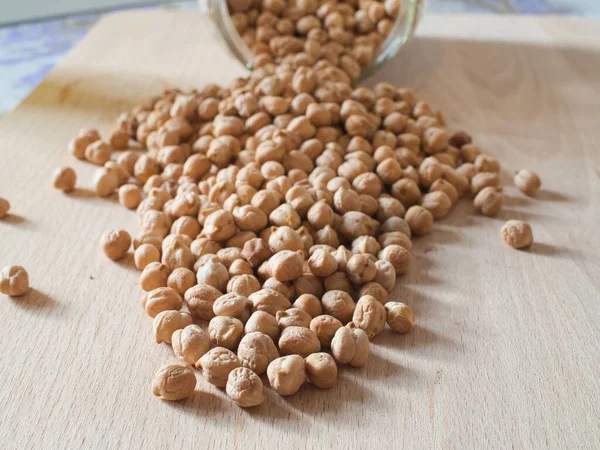 Group of raw and dried chickpeas come out of a glass jar and lie on a wooden chopping board