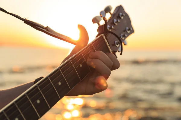 Genç adam (yumuşak odak günbatımında bir gitar çalmak)