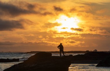 Fotoğrafçı silueti deniz kenarında gün doğumunun fotoğraflarını çekiyor.