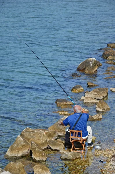 Homem velho pesca na costa — Fotografia de Stock