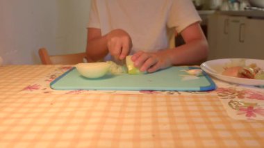 Sıcak bir mutfakta, bir insan taze sebzeleri soğan ve elma gibi keserek, dokularını ve renklerini göstererek ustalıkla yemek hazırlar.