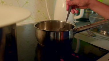 Bir insan yemek pişirir, ocakta demlik karıştırır, aşçılık hazırlıklarını yakalar ve bir mutfağın rahatlatıcı atmosferini yakalar.