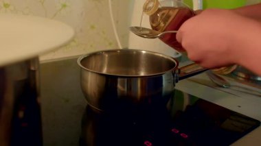 Bu yemek pişirme videosunda, bir kişi tencereye yağ ve şeker ekleyerek ustaca bir yemek hazırlıyor. Su karıştığında malzemeler karışır.