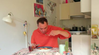 Sıcak bir mutfakta, kırmızı kapüşonlu bir adam besleyici yemeklerden ve renkli içeceklerden hoşlanır. Etrafı canlı mutfak malzemeleriyle çevrilidir. Rahatlamak için ideal, davetkar bir ortam yaratır.