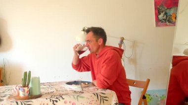 Bir adam rahat bir şekilde bir masada oturuyor, güzel bir tabak yemek ve ferahlatıcı bir içecek içeren lezzetli bir kahvaltıdan keyif alıyor, sıcak ev ortamında.