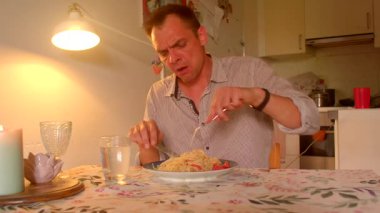 Bir adam, sıcak mum ışığında güzel bir sofrada leziz bir spagetti yemekten mutlu bir şekilde zevk alır. Keyifli yemek deneyimini mutfak ortamında sergiler.