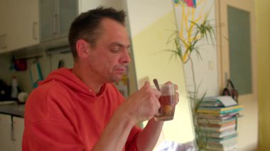 Bir adam rahat bir mutfak alanı işgal eder, lezzetli bir yemek ve sıcak bir fincan çay keyfini çıkarırken, bir dizi istiflenmiş kitap ve çeşitli mutfak malzemeleriyle çevrelenir.